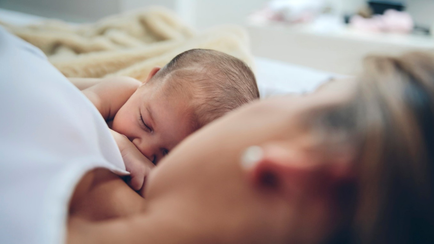 A mother lies in a bed gazing at her newborn snuggled next to her