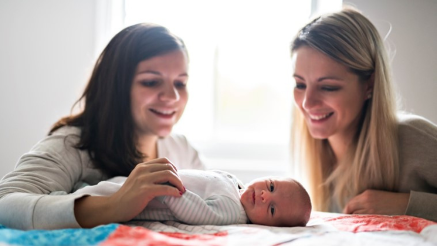 A mother and her friend look at her newborn lying in a cot